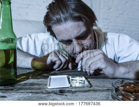 wasted alcoholic and drug addict man with loose tie snorting cocaine and drinking beer bottles at home living room couch in toxic substance addiction and abuse concept