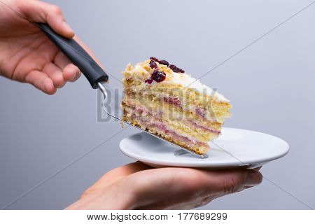 Cake with cherry on a white plate.waiter placing slice of cake to plate with cake server.