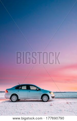 Gomel, Belarus - January 26, 2017: Volkswagen Polo Car Sedan Parking On A Snowy Roadside Of Country Road On A Background Of Dramatic Sunset Sky At Winter Season. There are spots of dirt on a car door