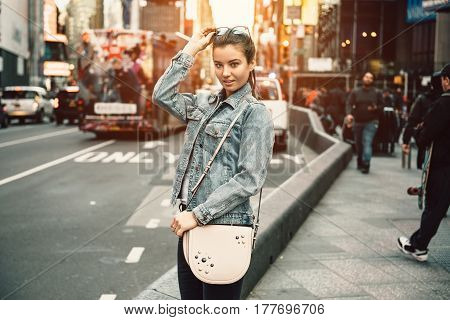 Lifestyle photo of happy young tourist adult woman looking at camera holding bag purse and sunglasses on sunny busy city street