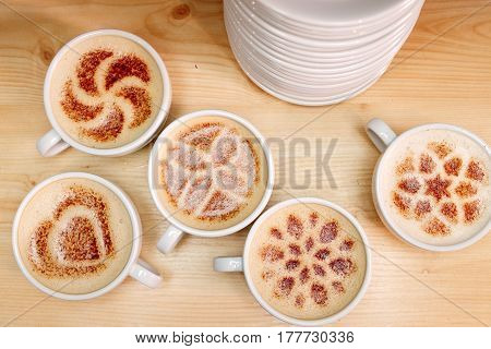 A lot of cups of coffee and a plate with a fire. Cappuccino coffee. A cup of latte, cappuccino or espresso coffee with milk put on a wood table. Drawing the foam milk on top.
