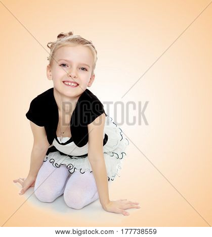Beautiful little blonde girl dressed in a white short dress with black sleeves and a black belt.The girl kneeling on the floor smiling directly into the camera.