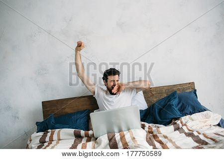 Handsome Man Sitting In Bed And Stretching