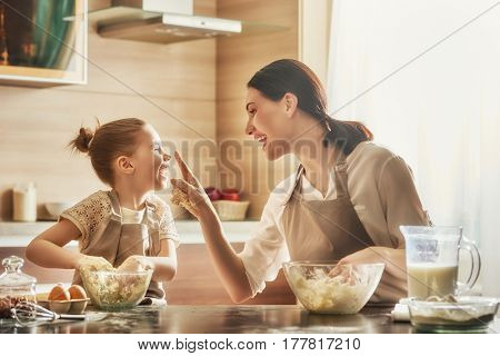 Happy loving family are preparing bakery together. Mother and child daughter girl are cooking cookies and having fun in the kitchen. Homemade food and little helper.