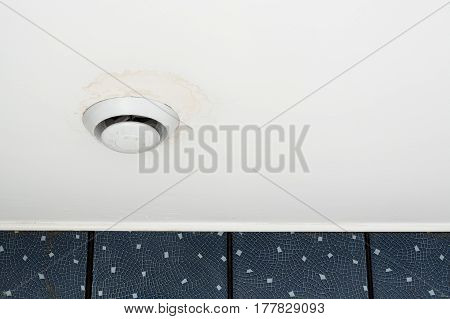 Round air ventilation frame on white ceiling with wet stains streaks and mould around ventilator.