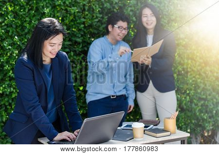 Asian Business Woman Using Computer Laptop And Her Team Dicussing Something While Working.