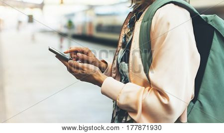 Enjoying travel. Young pretty woman waiting on the station platform with backpack on background electric train using smartphone. Tourist texting message and plan route of railway railroad transport concept