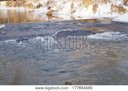 Spring ice melts on the river. Reflection of a tree in water. evening in the forest. Sun rays and colorful clouds. Flooding. A view from below on snow and ice on the river. Thaw in early spring.