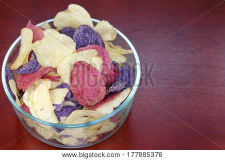Crimson Yellow and Purple Potato Chips Crimson Purple Majesty and Chipeta or Atlantic potato chips in a glass bowl on a wood table. Potato chips variety mostly referred to as red white and blue.