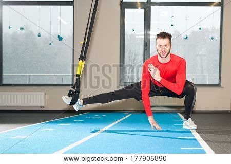white curly bearded sporty man exercising with fitness straps in gym.