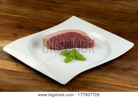 Slice Of Fresh Raw Cow Beef (picanha) And Basil Leaves On A White Dish And Vintage Natural Wood Tabl