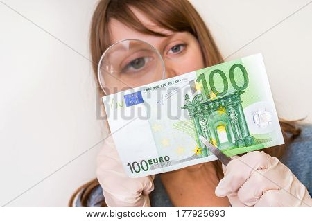 Woman Viewing Counterfeit Banknote With Magnifying Glass