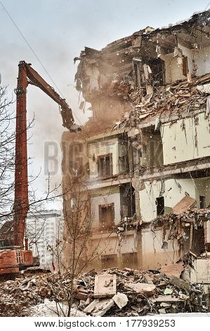 Builders demolishes a city house using an excavator equipped with special hydraulic scissors