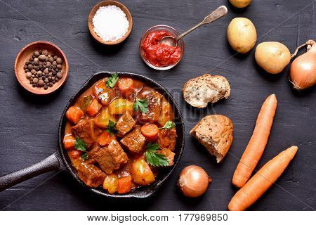 Goulash beef stew and ingredients on dark background top view