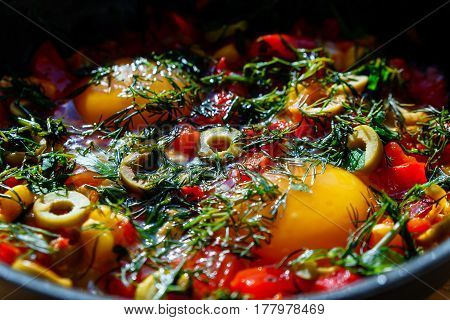 Egg in a frying pan with olives pepper and greens