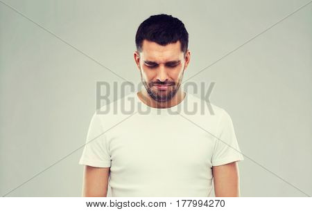 emotion, sadness and people concept - unhappy young man over gray background