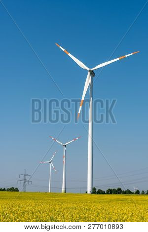 Yellow Blossoming Rapeseed And Wind Energy Turbines Seen In Rural Germany