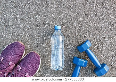 Two Dumpbells And Bottle Of Water Are Lying Near Purple Sneakers