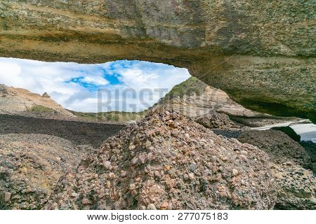 Landscape Through Natural Arch Rock And Stone Geological Structure To Cloudy Sky At Wharariki On Sou