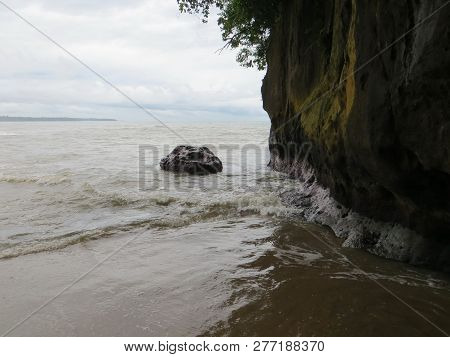 Anyer, Indonesia - June 25, 2018: The Waves Crashing Into The Large Rock On The Beach.