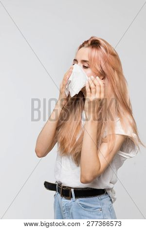 Portrait of young beautiful woman blowing her nose into a paper napkin, looking on the left/cold, sneezing, allergy symptoms, flu, rhinitis, sickness, desperately sick, healthcare and medicine concept.
