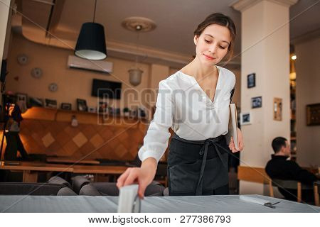 Nie Waitress Stand At Table And Prepare It For Customers. She Look Down. Young Woman Hold Notebook I