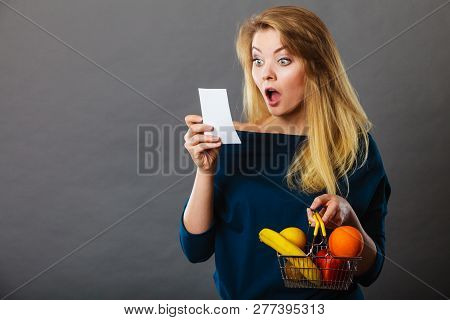 Shocked Woman Holding Shopping Basket With Fruits Looking At Bill Receipt Being Scared Of Huge Price