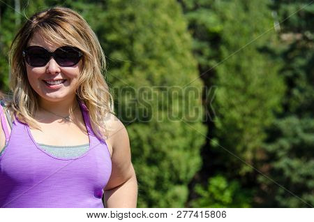 Portrait Of A Young Adult Woman Wearing Sunglasses And Smiling Next To A Rocky Background