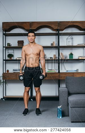 Muscular Bi-racial Man Standing With Heavy Dumbbells In Living Room