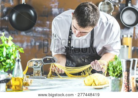 Chef Making Spaghetti Noodles With Pasta Machine On Kitchen Table With Some Ingredients Around