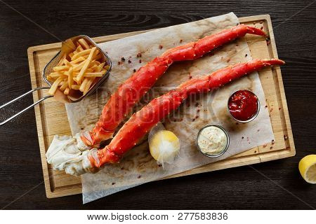 Alaskan King Crab Legs With Butter And Tomato Sauces And French Fries Served On Wooden Board, Top Vi