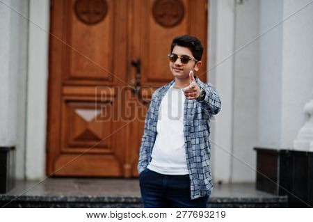Stylish Indian Young Man At Sunglasses Wear Casual Posed Outdoor Against Door Of Building, Show Fing