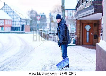 Man With Snow Shovel Cleans Sidewalks In Winter During Snowfall. Winter Time In Europe. Young Man In
