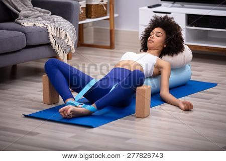 Relaxed Young Woman Lying On Fitness Mat Doing Exercise With Yoga Belt And Two Blocks