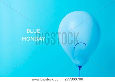 closeup of a blue balloon, with a sad face drawn in it, and the text blue monday on a blue background