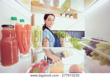 Portrait Of Female Standing Near Open Fridge Full Of Healthy Food, Vegetables And Fruits. Portrait O