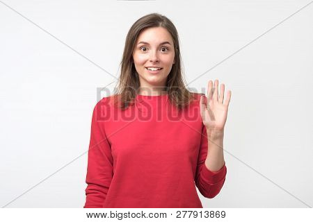 Friendly-looking Teenager Dressed In Red Pulover Saying Hello, Waving Her Hand.