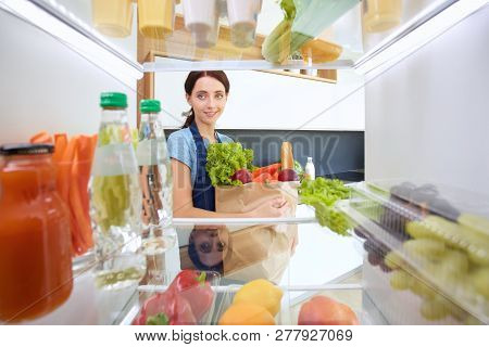 Portrait Of Female Standing Near Open Fridge Full Of Healthy Food, Vegetables And Fruits. Portrait O