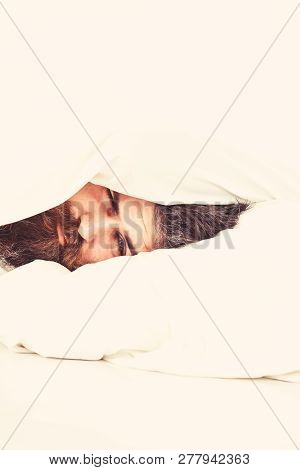 Man With Drowsy Face Lies On Pillow Under Blanket.