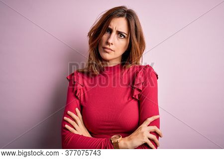 Young beautiful brunette woman wearing casual sweater stnding over pink background skeptic and nervous, disapproving expression on face with crossed arms. Negative person.
