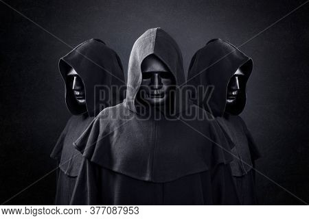Group of three scary figures in hooded cloaks in the dark