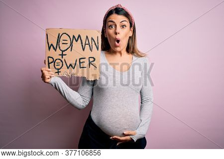 Young brunette woman pregnant expecting baby holding banner asking for women power scared in shock with a surprise face, afraid and excited with fear expression