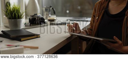 Female Photographer Using Digital Tablet While Sitting At Worktable With Supplies, Camera And Decora