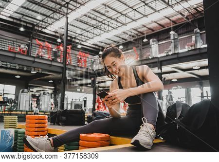 Sporty Woman Using Mobile Phone After Workout. Asian Woman Exercise And Lifestyle At Fitness Gym. We