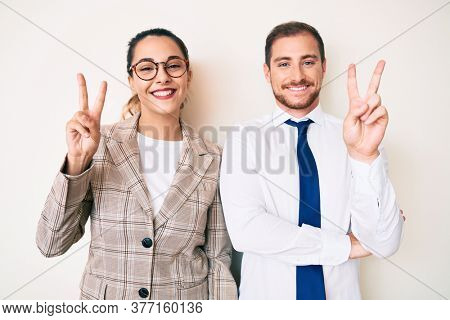 Beautiful couple wearing business clothes smiling looking to the camera showing fingers doing victory sign. number two. 