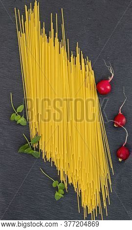 Raw pasta on the table with vegetables, papryka, radish and mint.