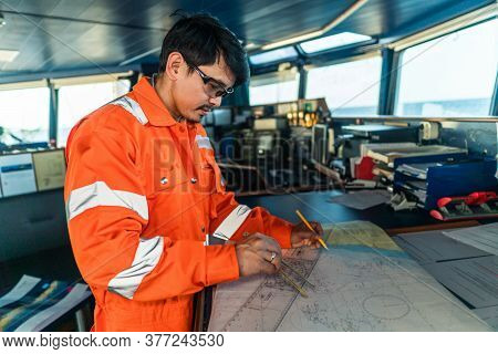 Filipino Deck Officer On Bridge Of Vessel Or Ship. He Is Plotting Position On Chart