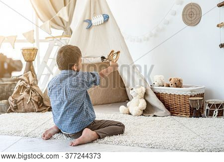 Back view of little boy shooting paper target with slingshot sitting on floor in kids room