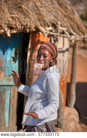 african woman dancing holding a twenty pula note in her mouth in front of her house