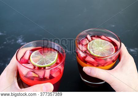 Man And Woman's Hand Holding A Glass Of Homemade Red Wine Sangria On Black Marble Table